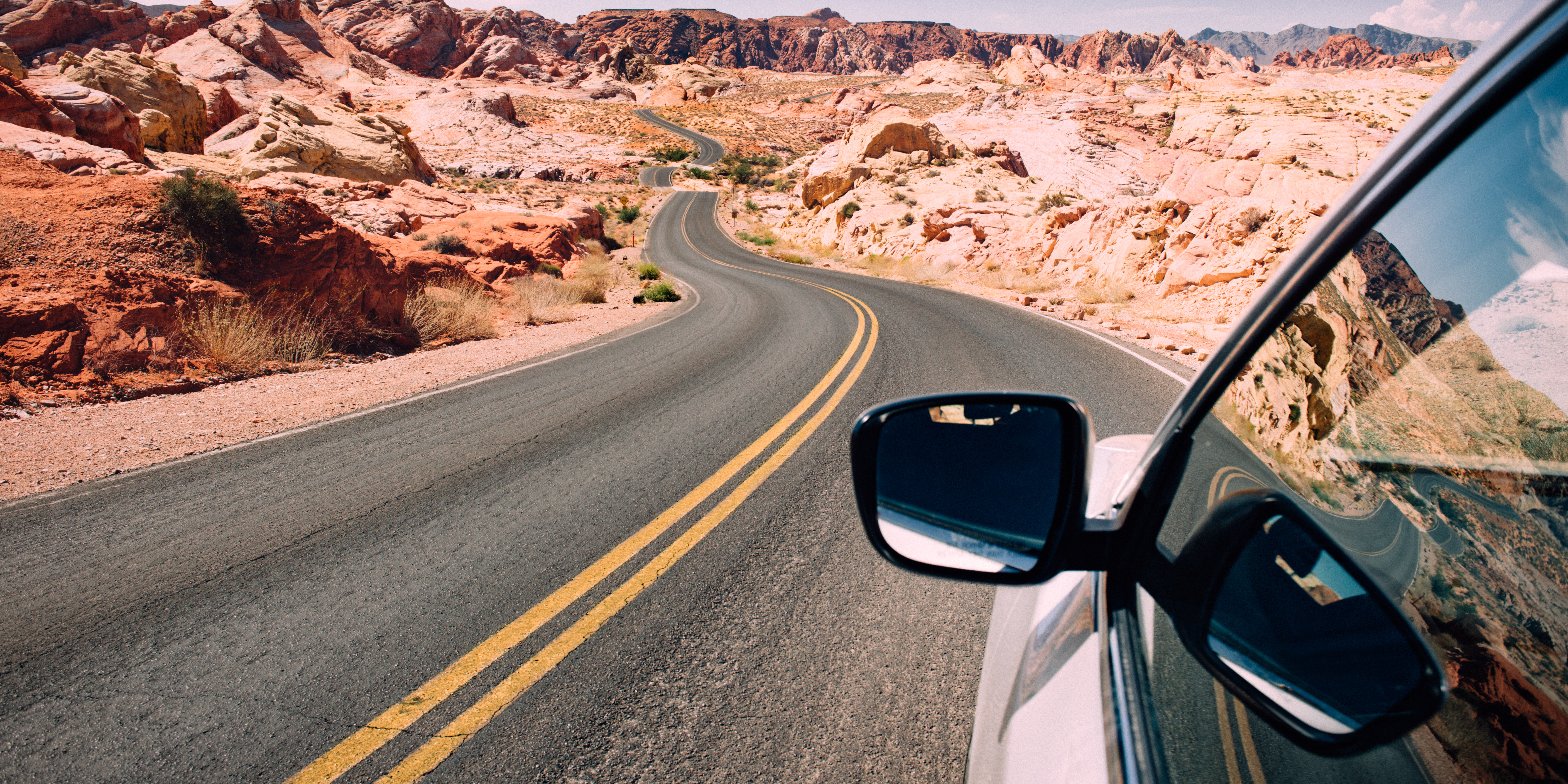 A car driving through a winding desert highway surrounded by red and tan rock formations, symbolizing navigating the journey ahead.