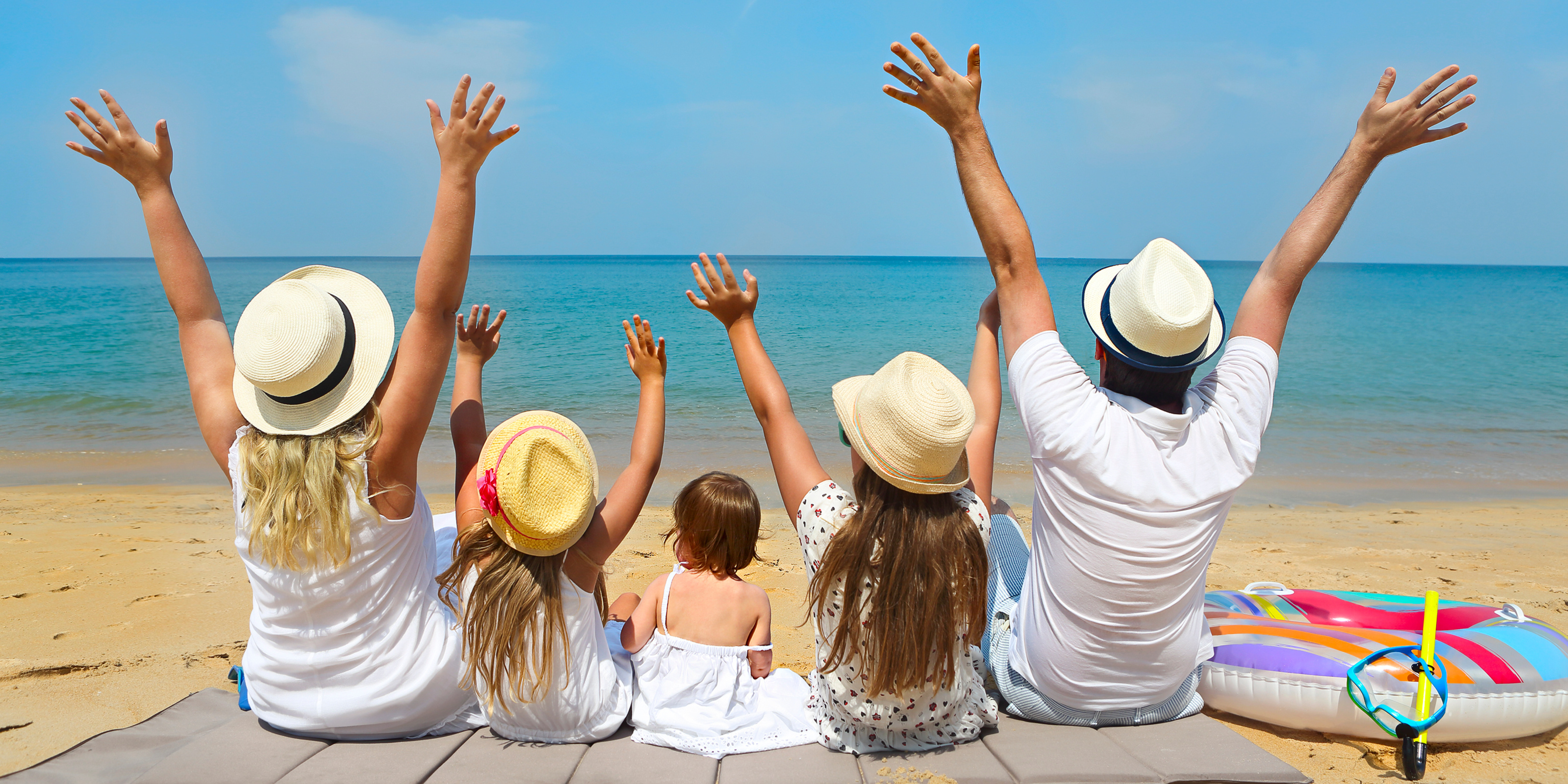 Family sitting together on the beach with their hands raised toward the ocean, symbolizing summer fun, co-parenting balance, and preparation for the back-to-school season.