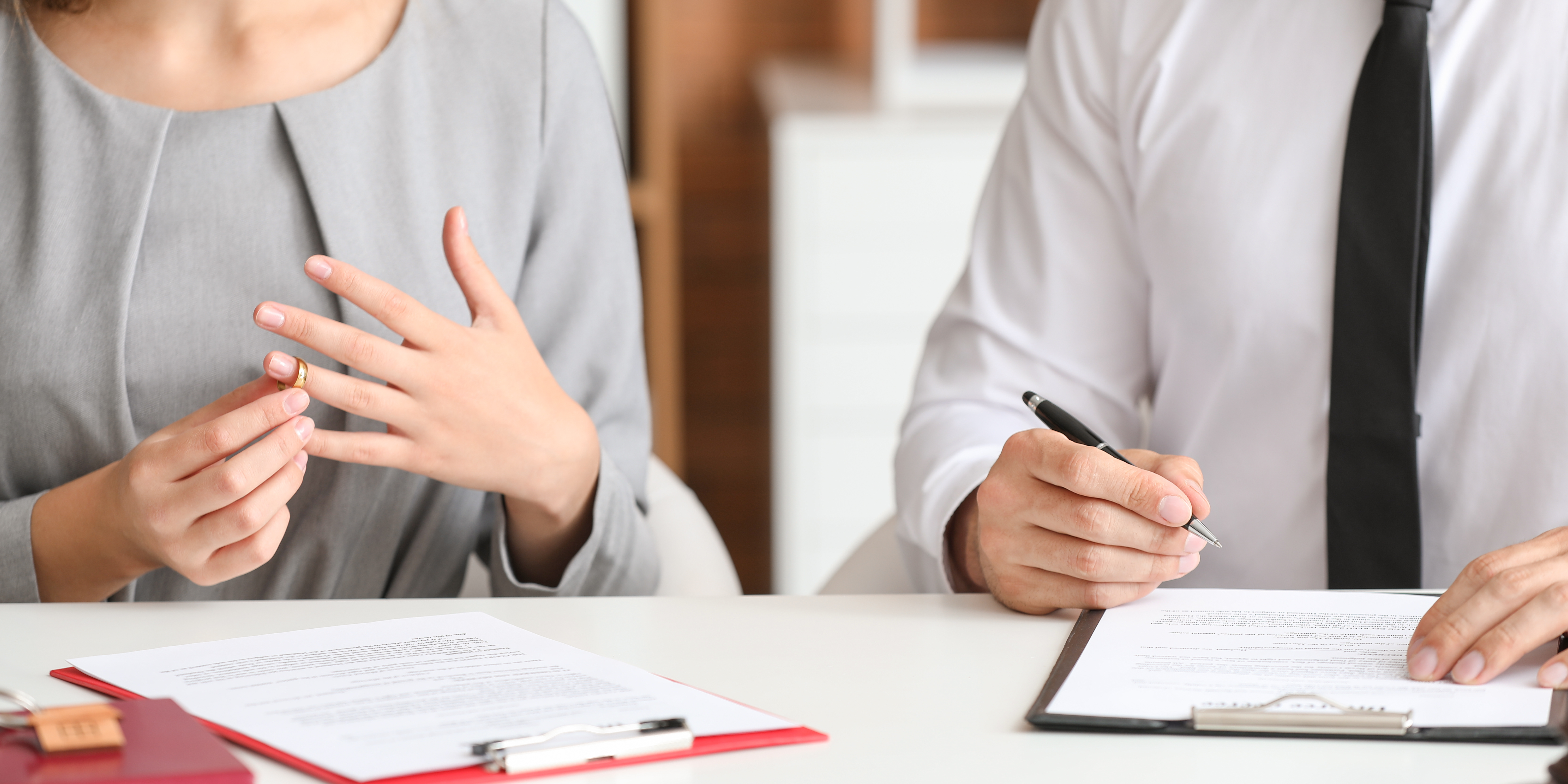 Close-up of a woman removing her wedding ring while sitting with legal documents and a professional, symbolizing communication and decision-making during divorce proceedings.