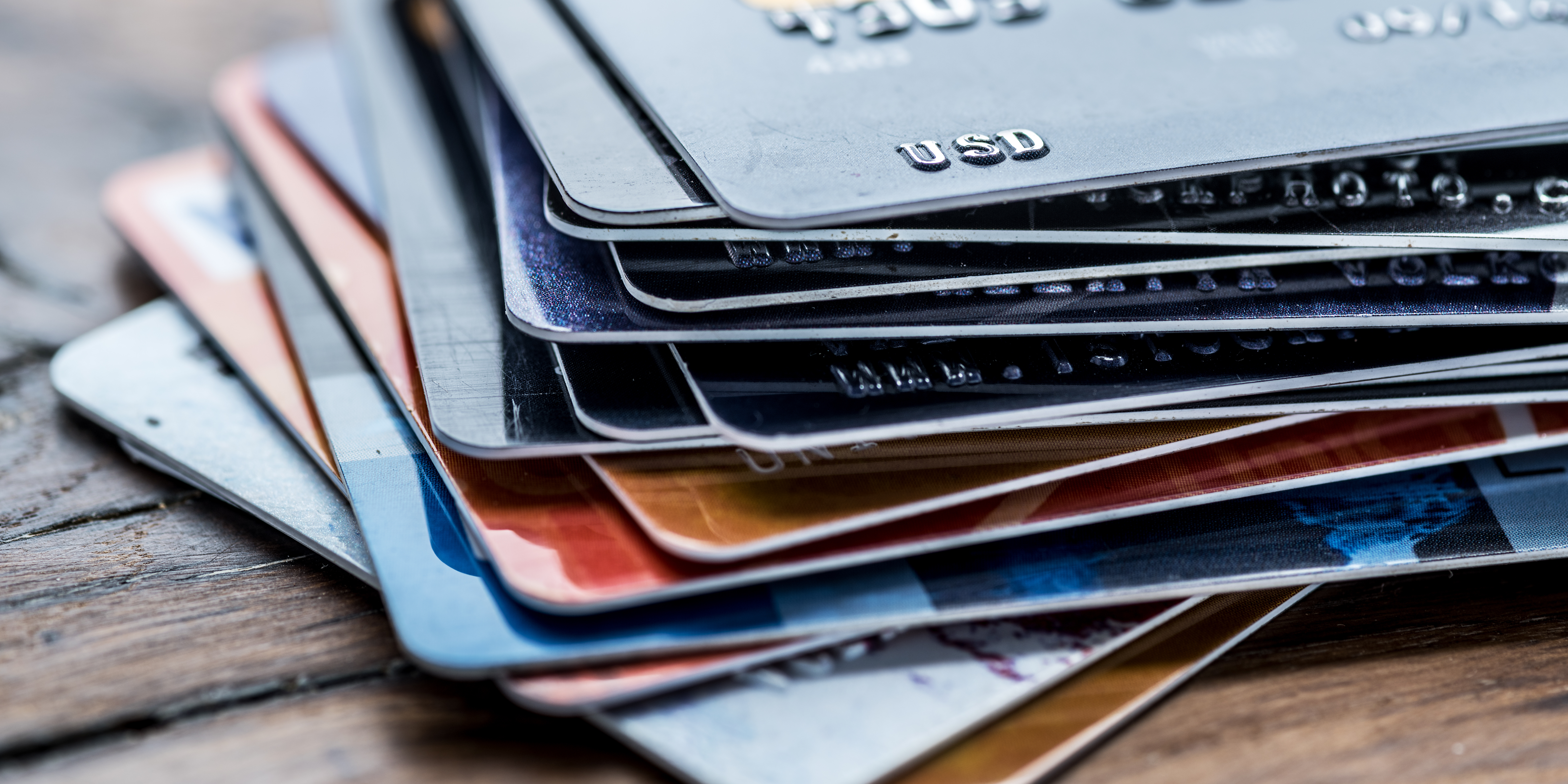 A close-up stack of various credit cards piled on a wooden table.