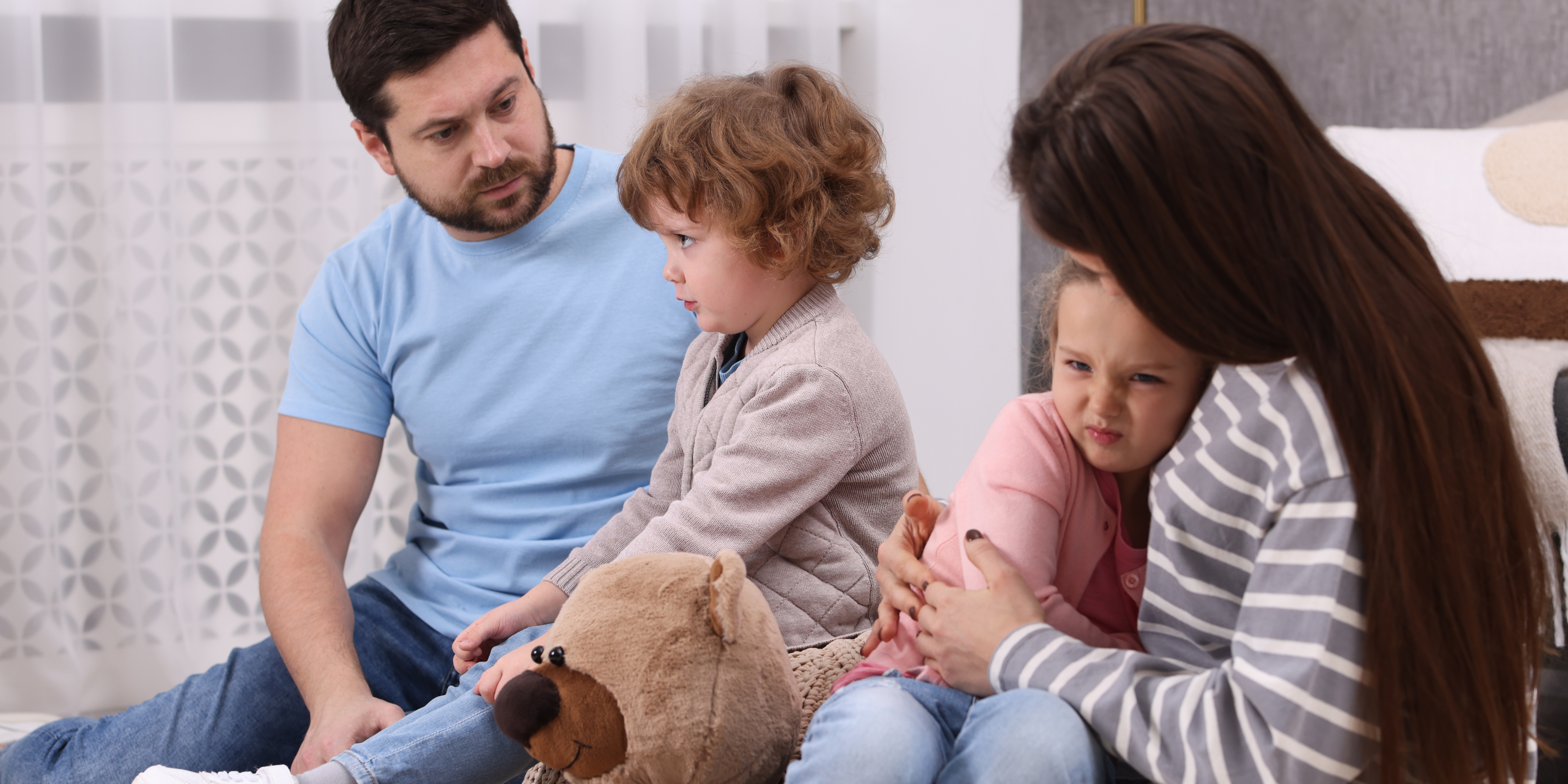 Two parents sitting with their young children, who appear upset, during a difficult family discussion.