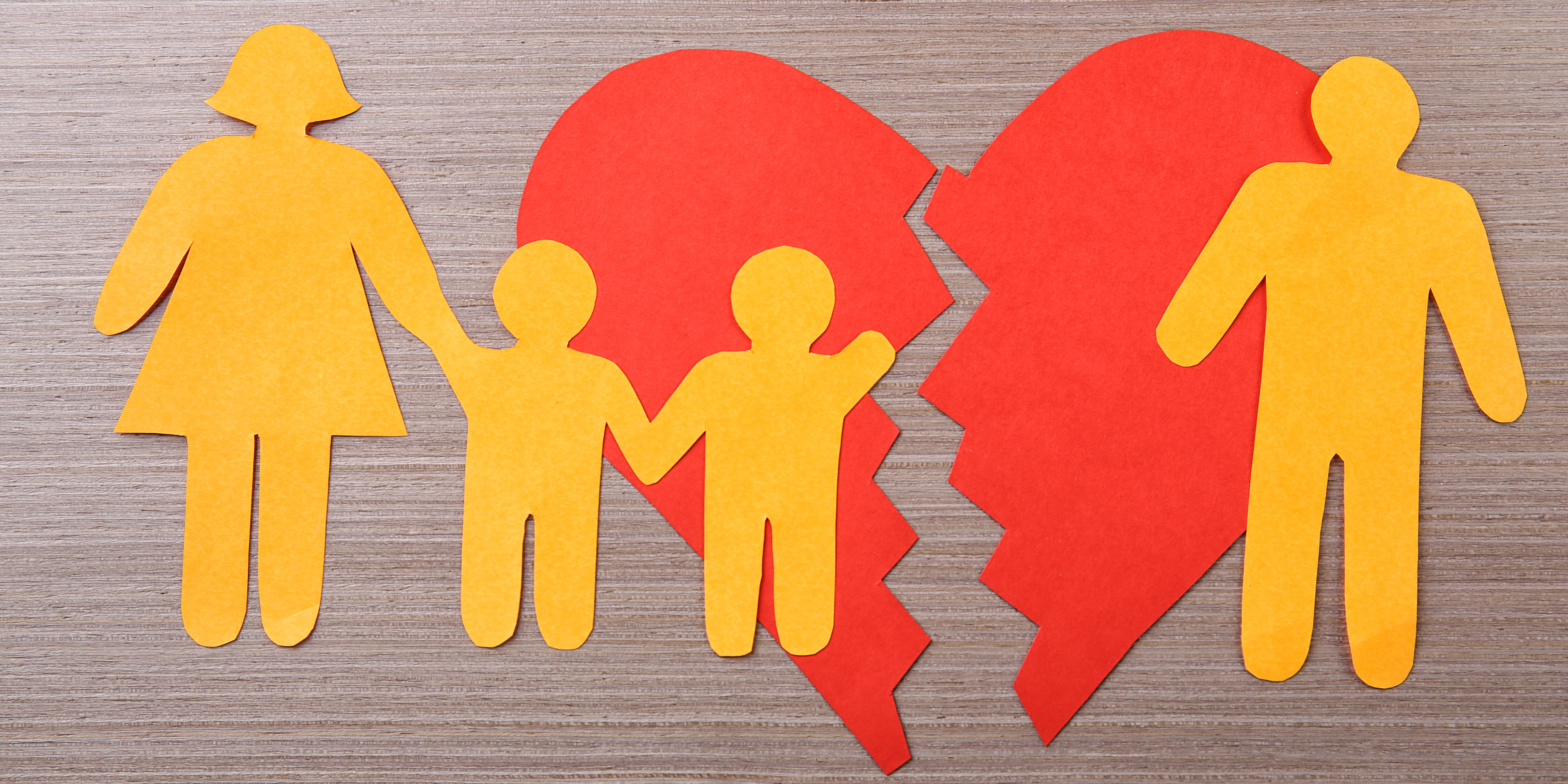 Paper cutout of a divided family standing in front of a broken red heart, symbolizing co-parenting challenges after divorce.