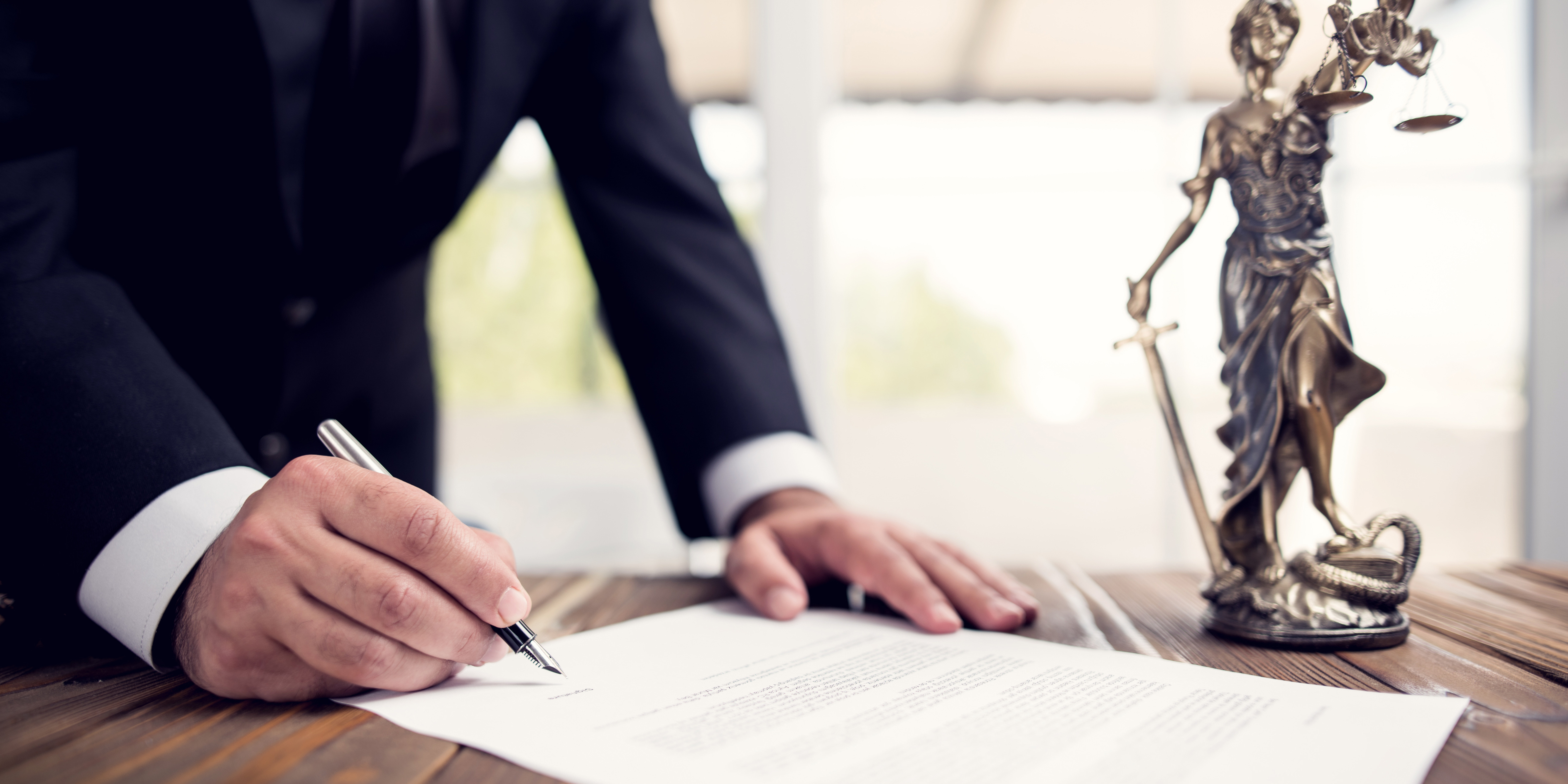 Close-up of a lawyer signing legal documents beside a Lady Justice statue, symbolizing informed decision-making and legal guidance before signing agreements.