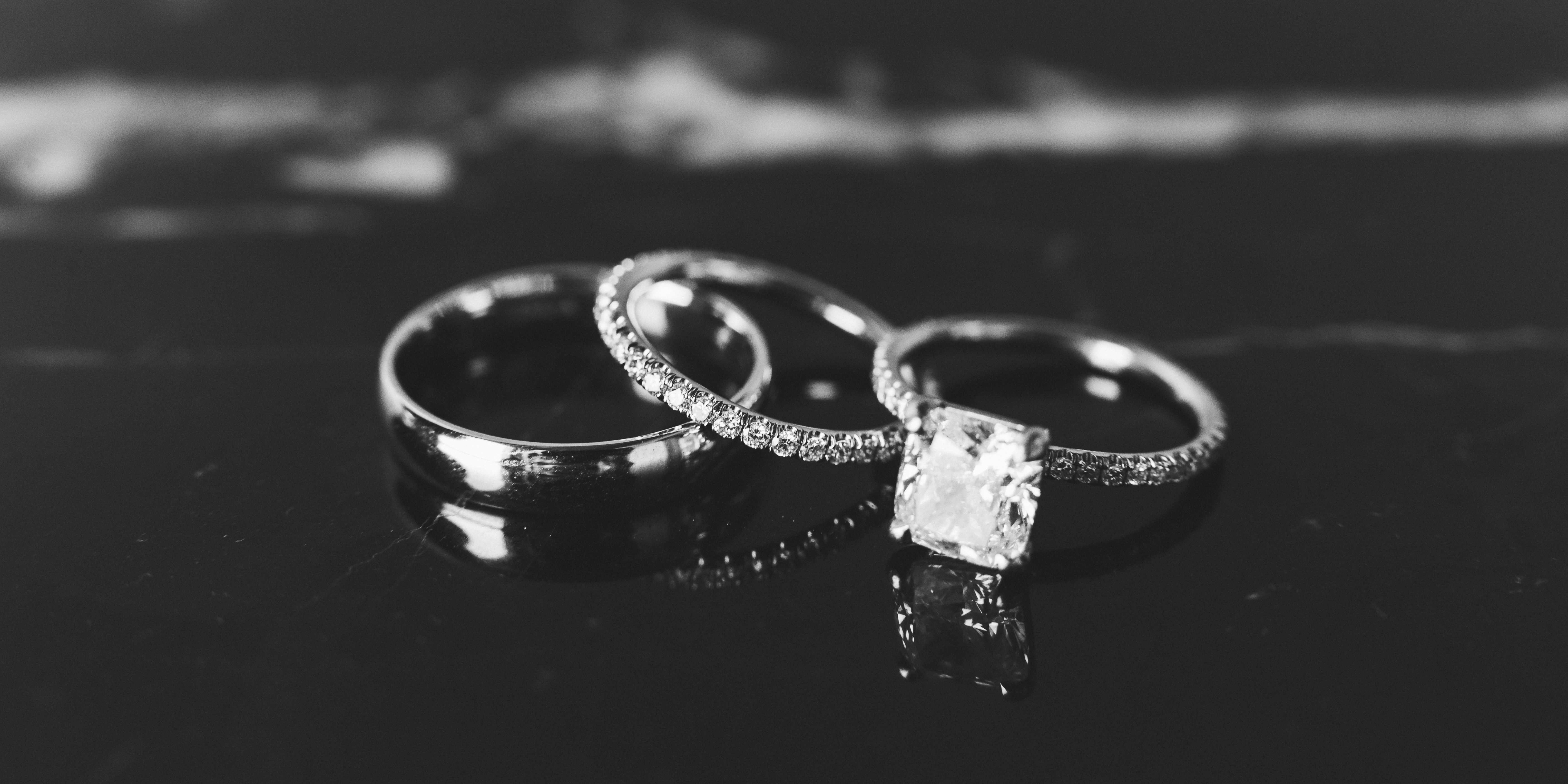 A close-up of wedding and engagement rings placed together on a reflective black background.