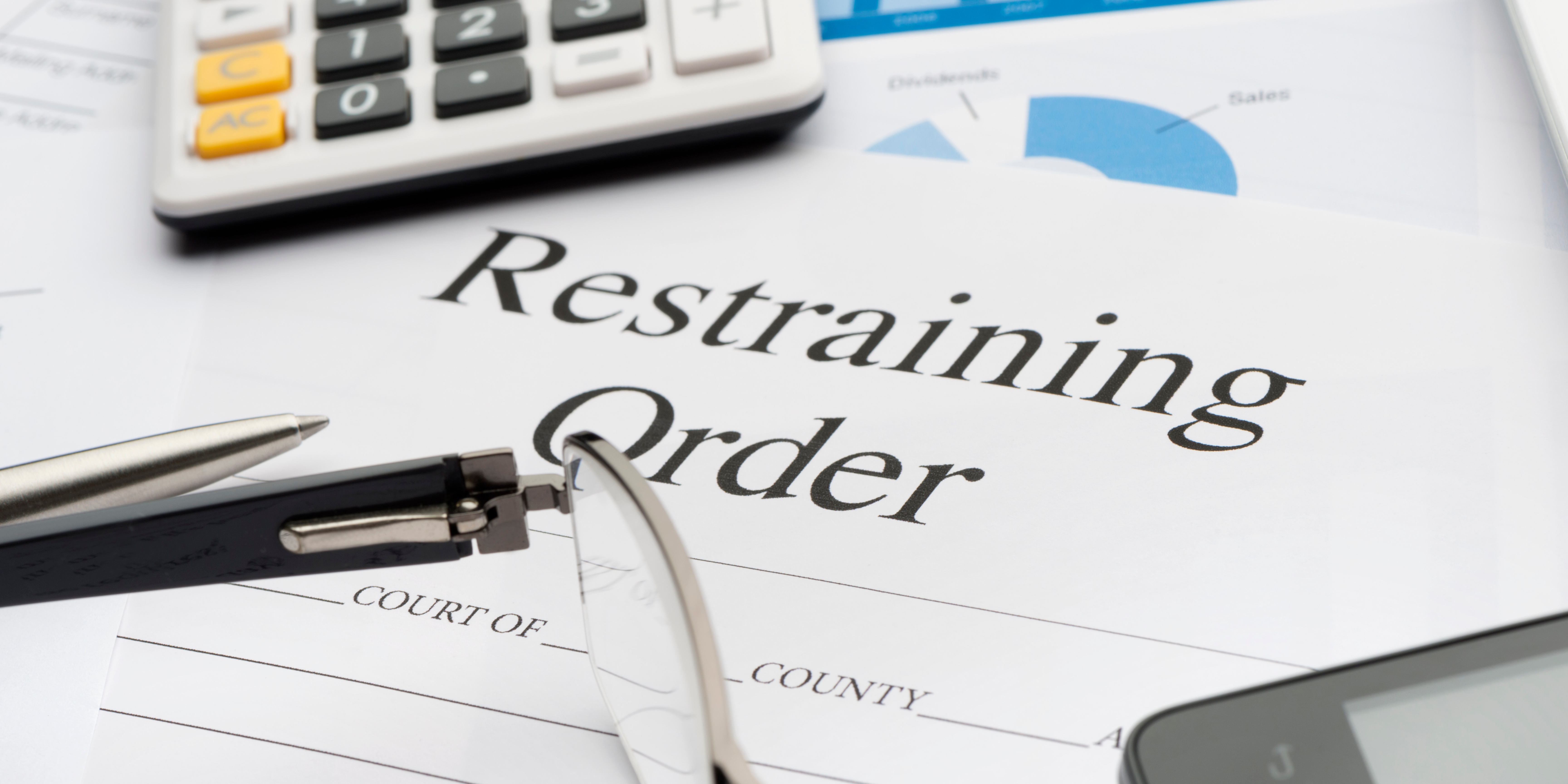 A close-up image of a California domestic violence restraining order form with a pen, eyeglasses, and calculator resting on top, symbolizing legal protection, court filings, and family law matters involving Domestic Violence Restraining Orders (DVROs).