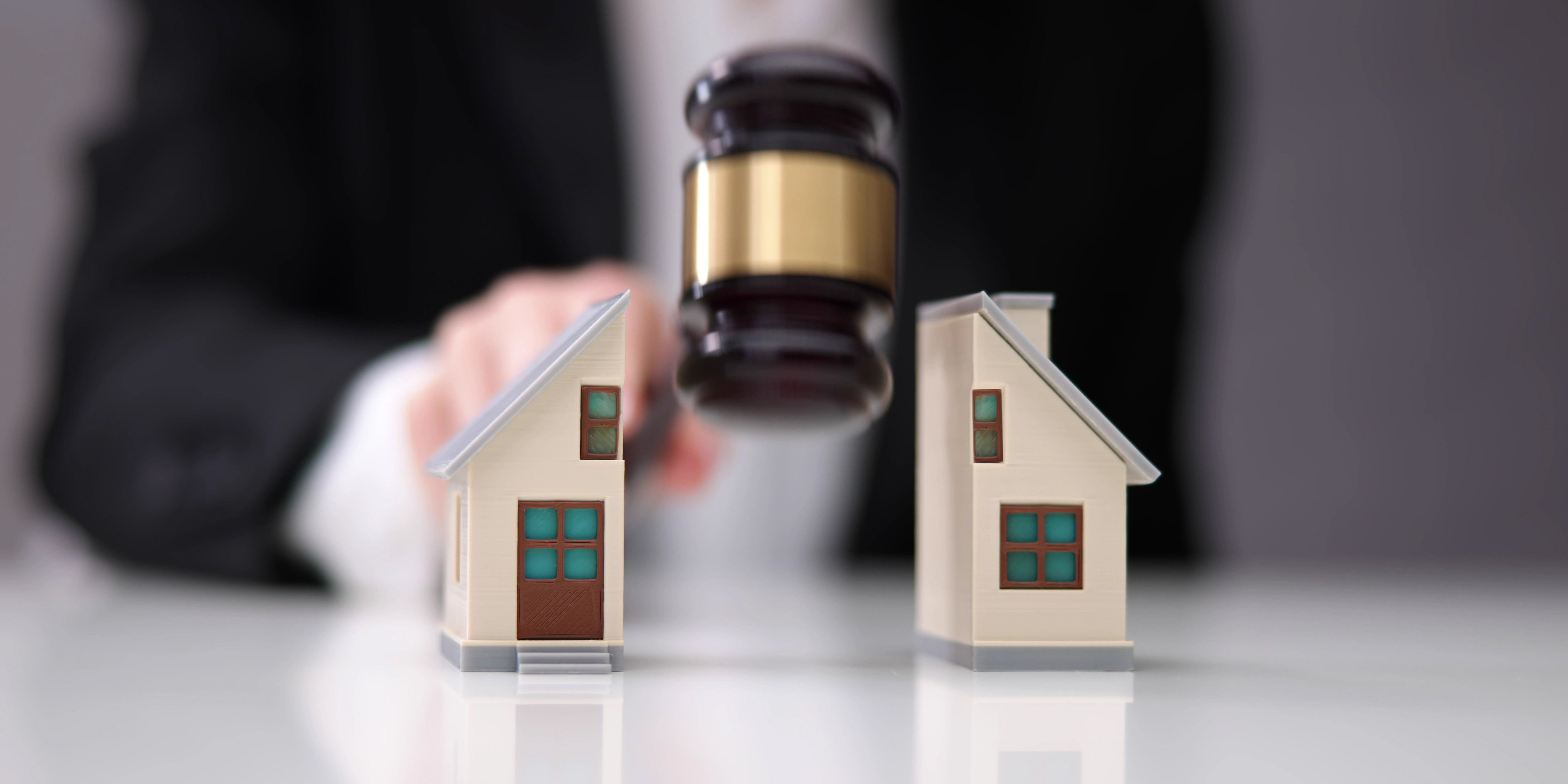 Close-up of a judge’s gavel dividing two miniature houses on a desk, symbolizing property division in divorce or family law proceedings.