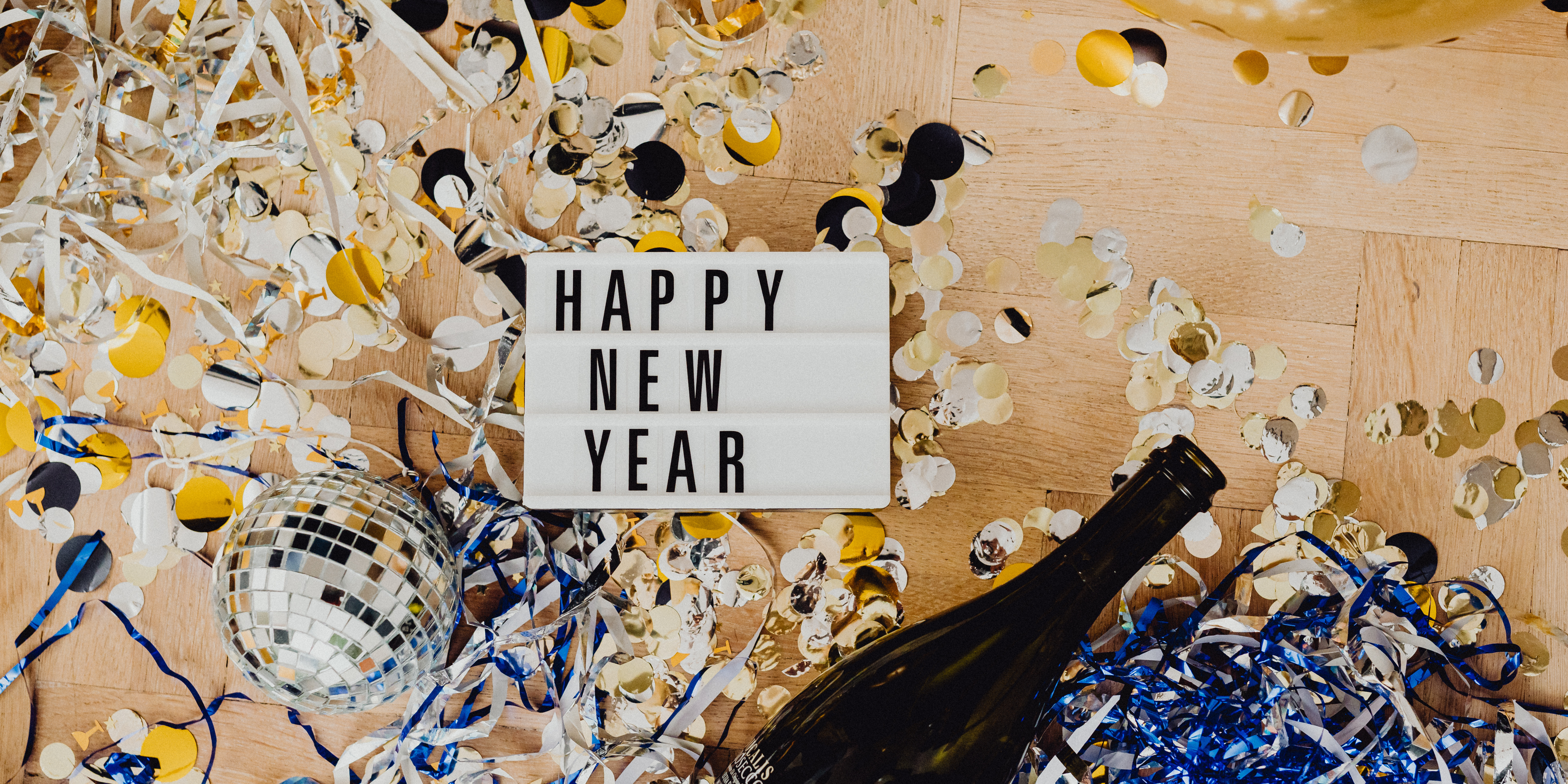 A celebratory New Year scene with confetti, streamers, a disco ball, and a sign reading “Happy New Year.”