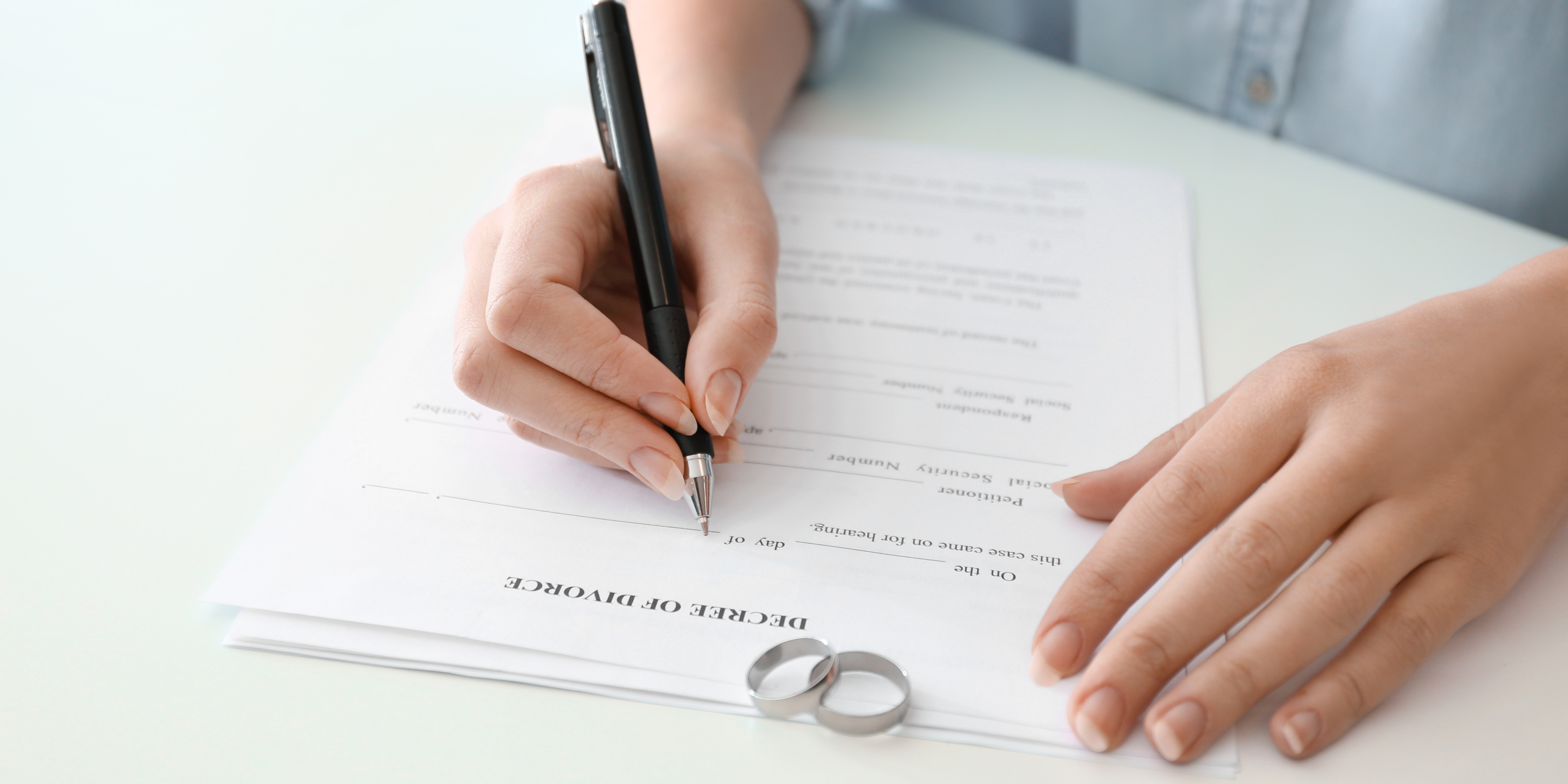 Close-up of a woman signing divorce papers beside two wedding rings, symbolizing personal choice and identity during and after divorce.