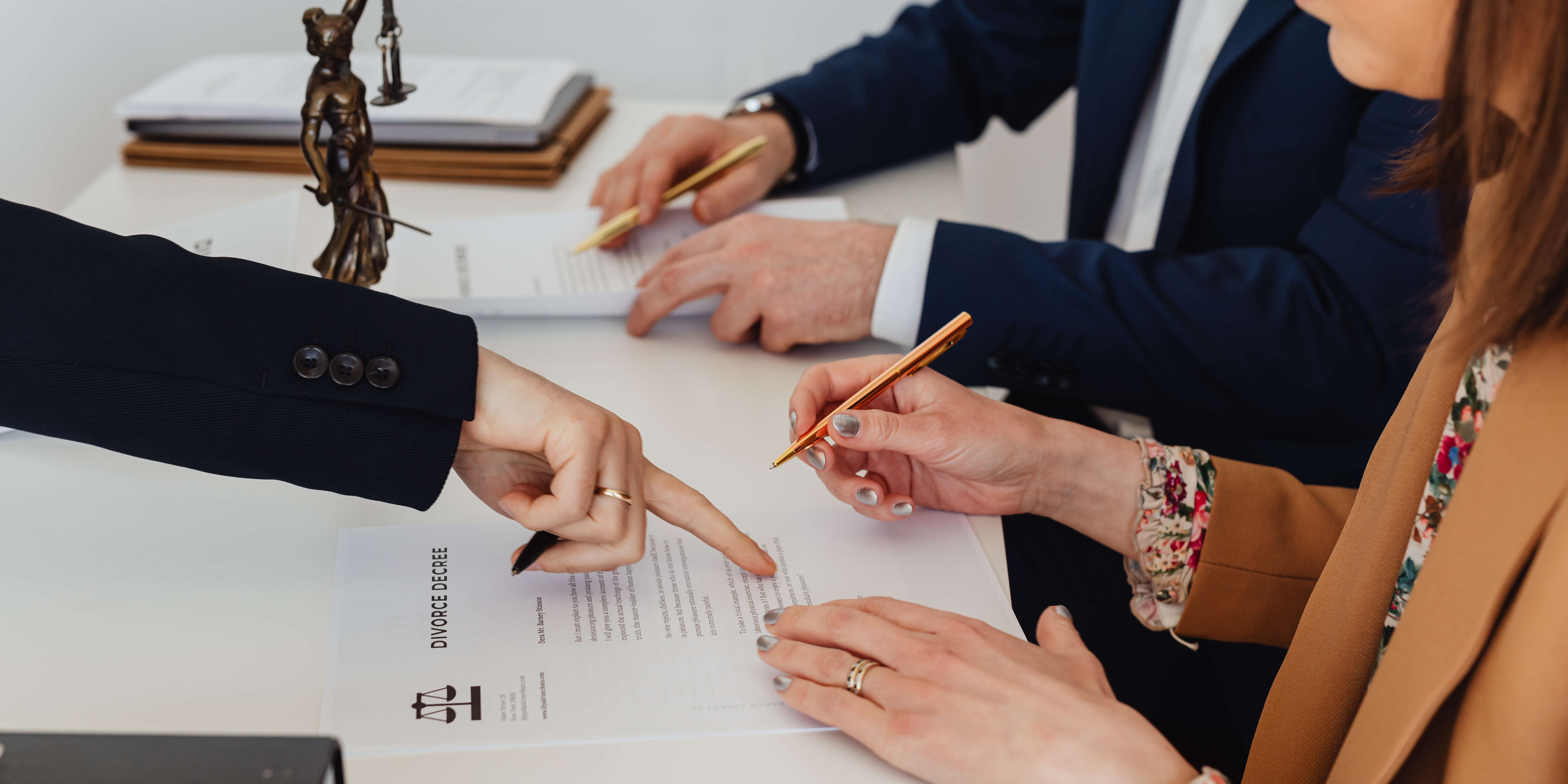 A couple signs divorce papers at a lawyer’s office while reviewing documents labeled “Divorce Decree.”