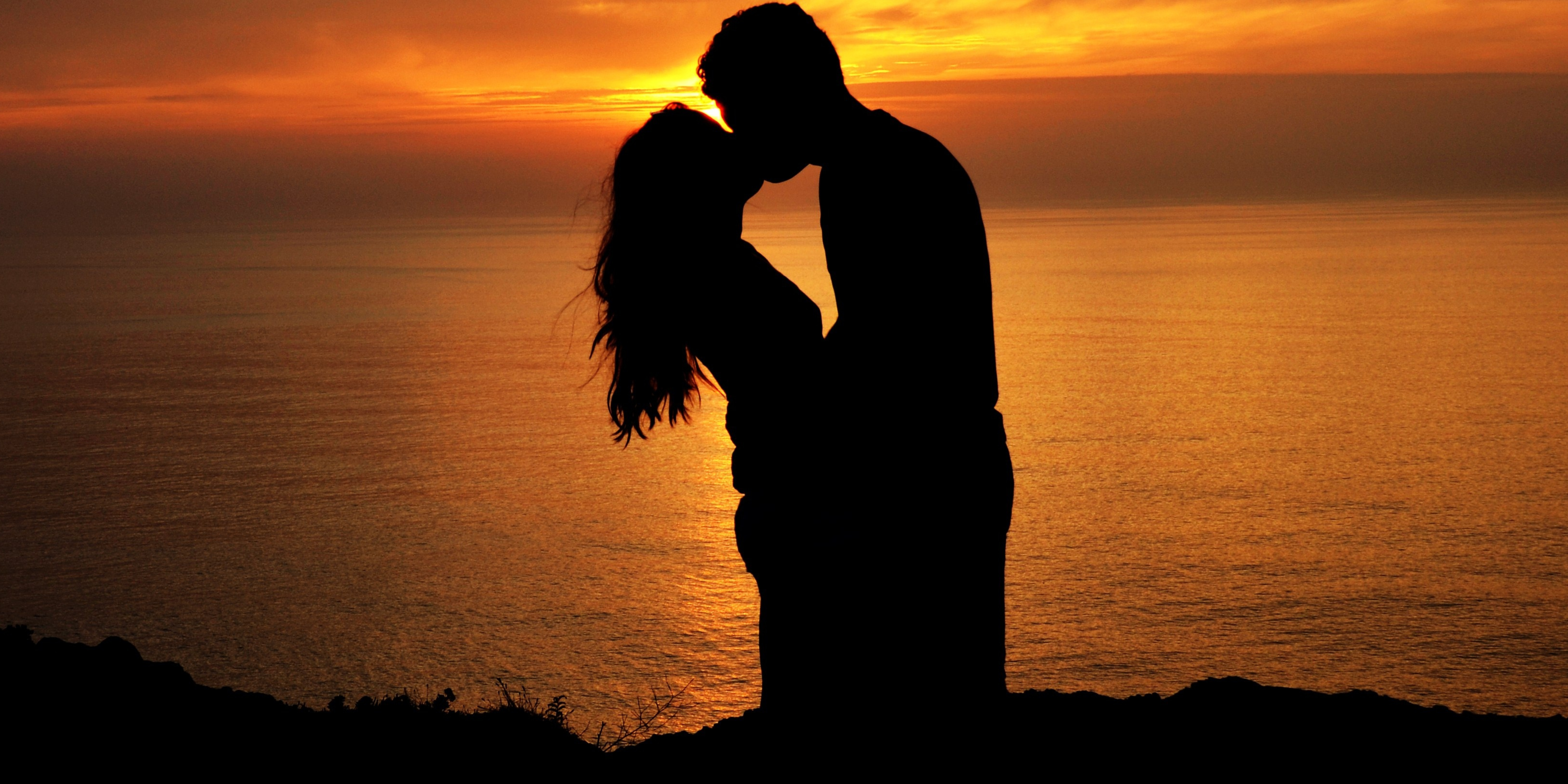 Silhouette of a couple sharing a kiss at sunset by the ocean, symbolizing love, connection, and relationship reflection.