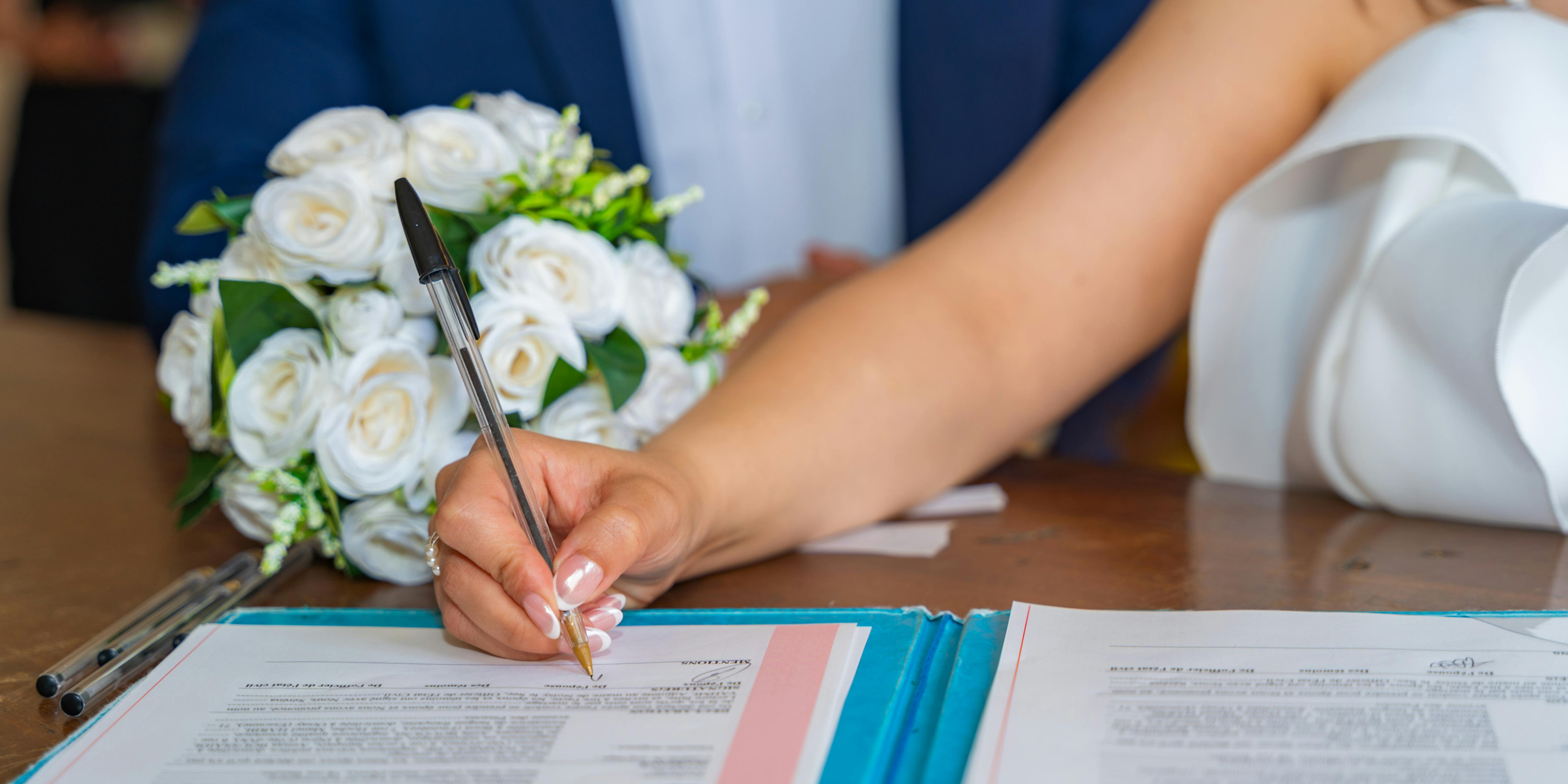 Bride signing a prenuptial agreement while holding a bouquet, symbolizing financial planning before marriage in California.