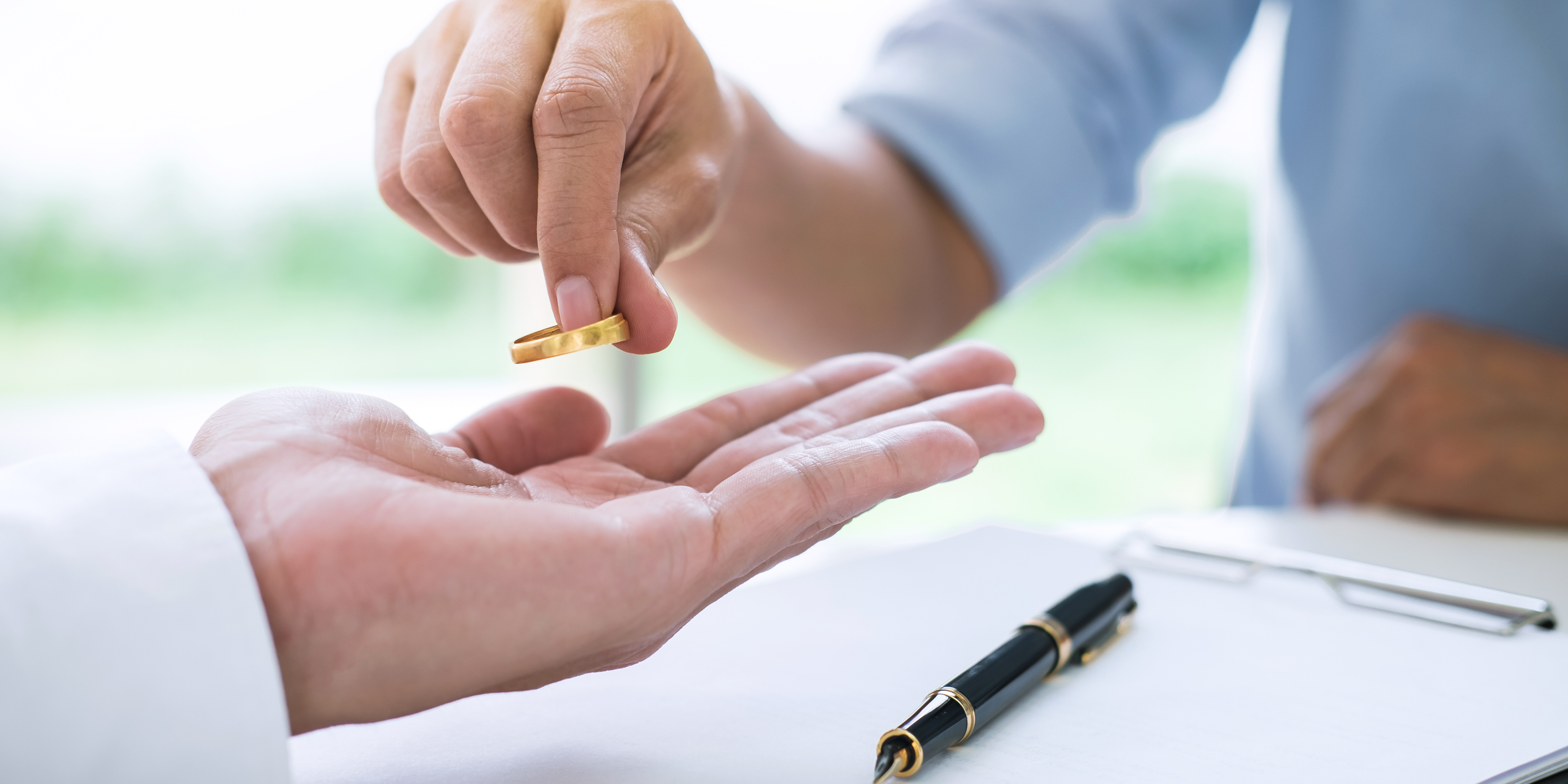 Close-up of a person handing back a wedding ring over divorce papers, symbolizing the decision to end a marriage and prepare for a new beginning.