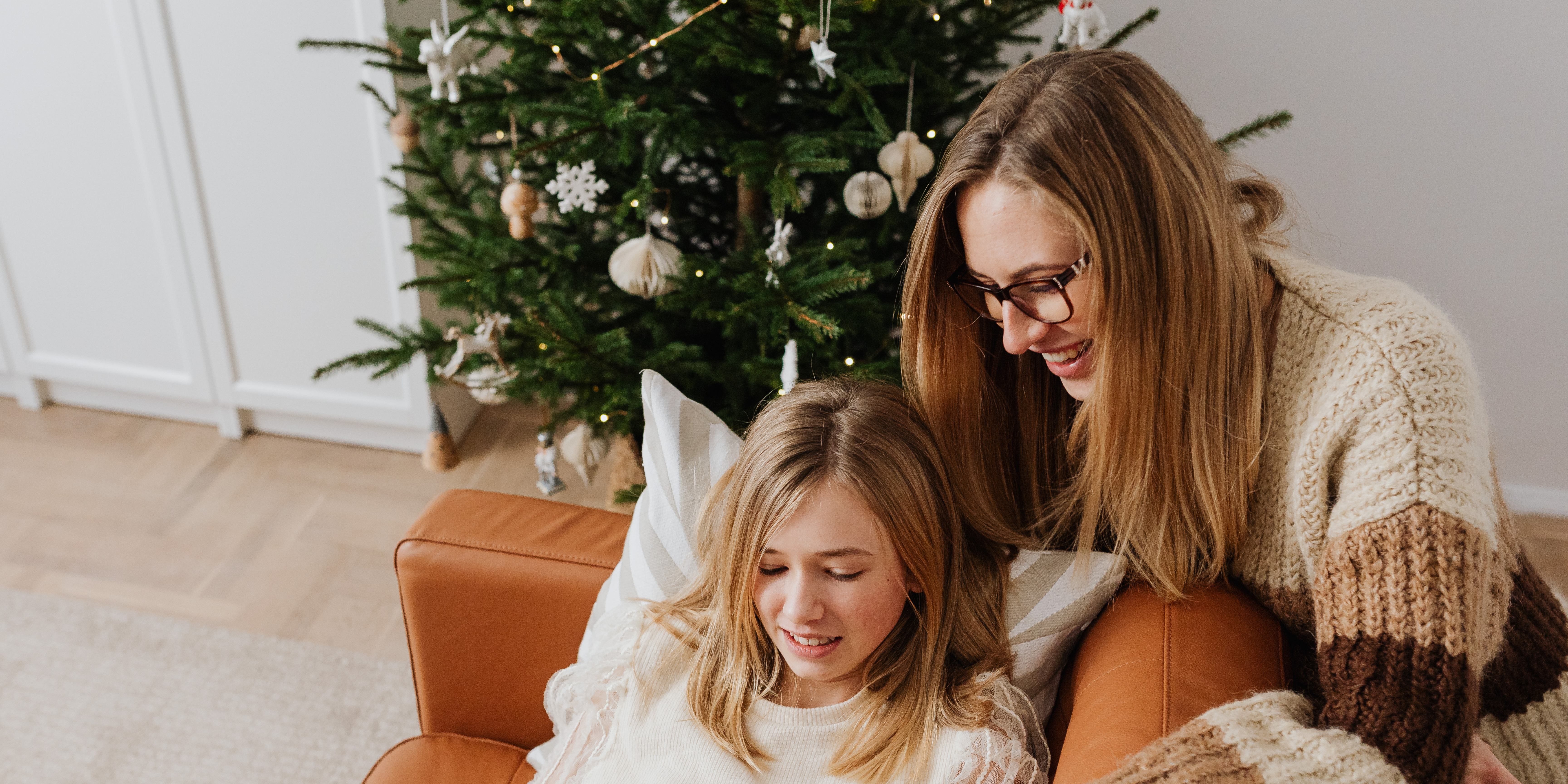 A parent and child relax together by the Christmas tree, sharing a warm holiday moment at home.