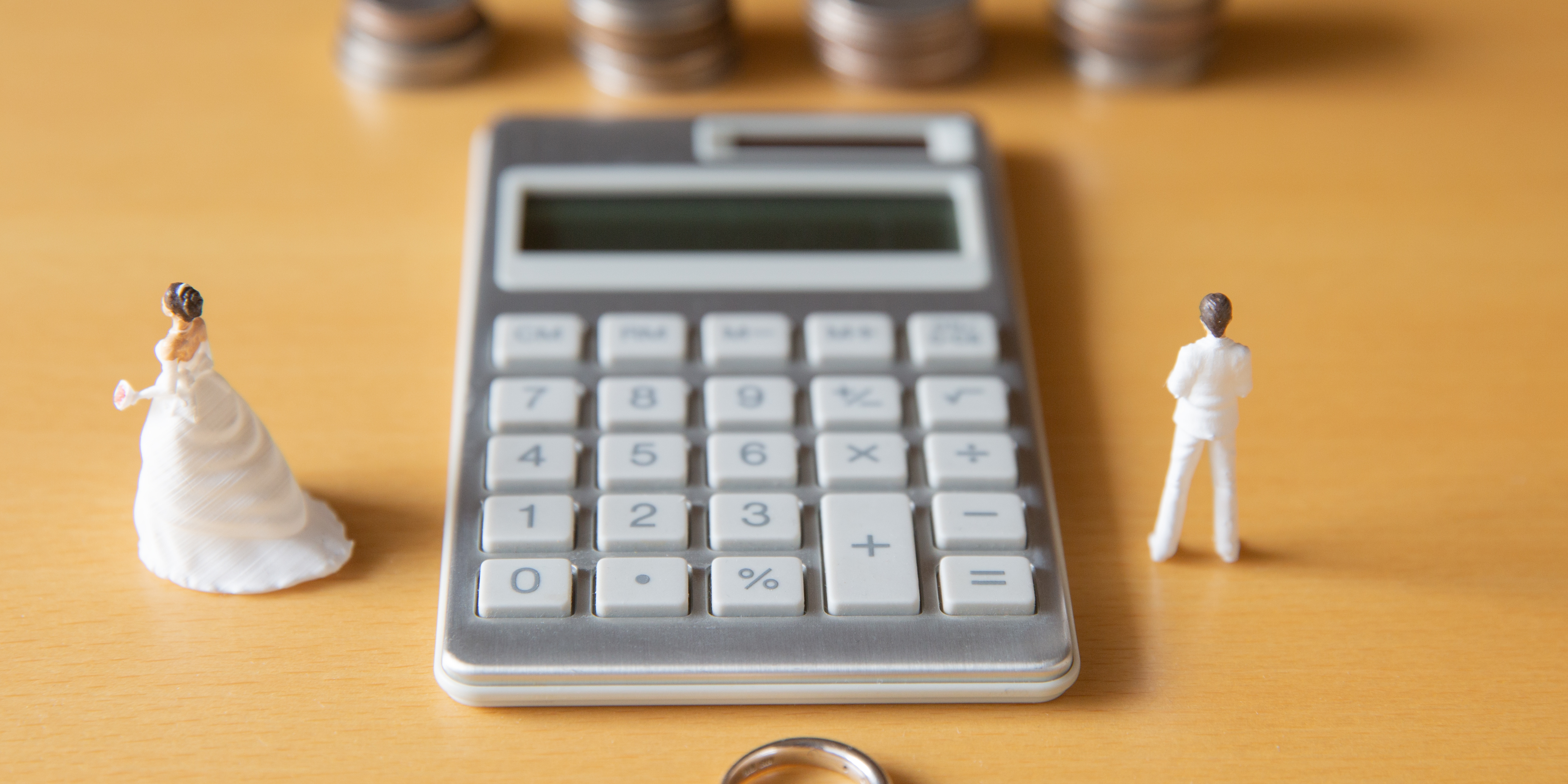 A calculator on a table with miniature bride and groom figures standing apart, symbolizing financial challenges during divorce.