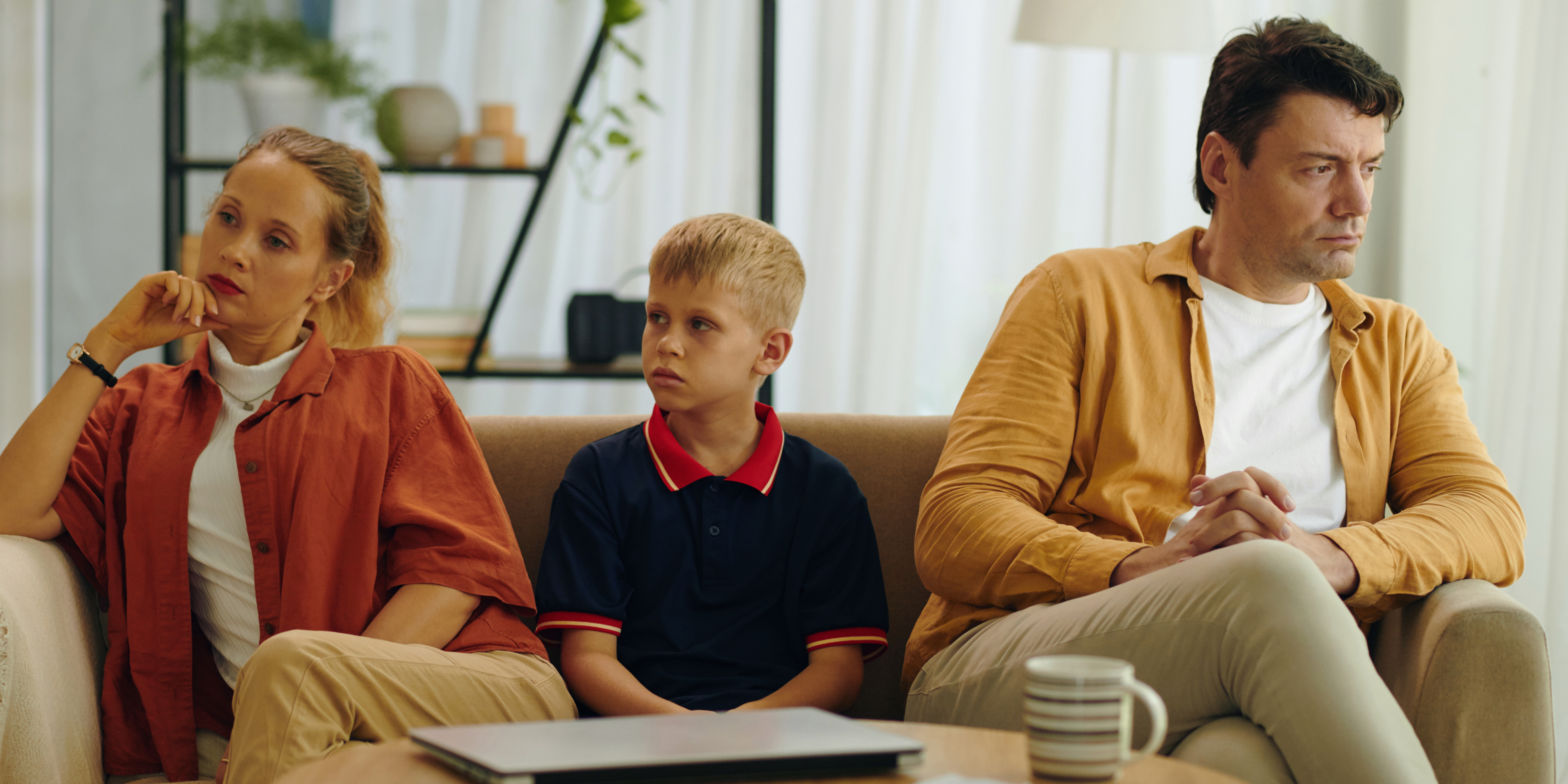 A child sitting between two solemn parents on a couch, symbolizing custody decisions and parental conflict.