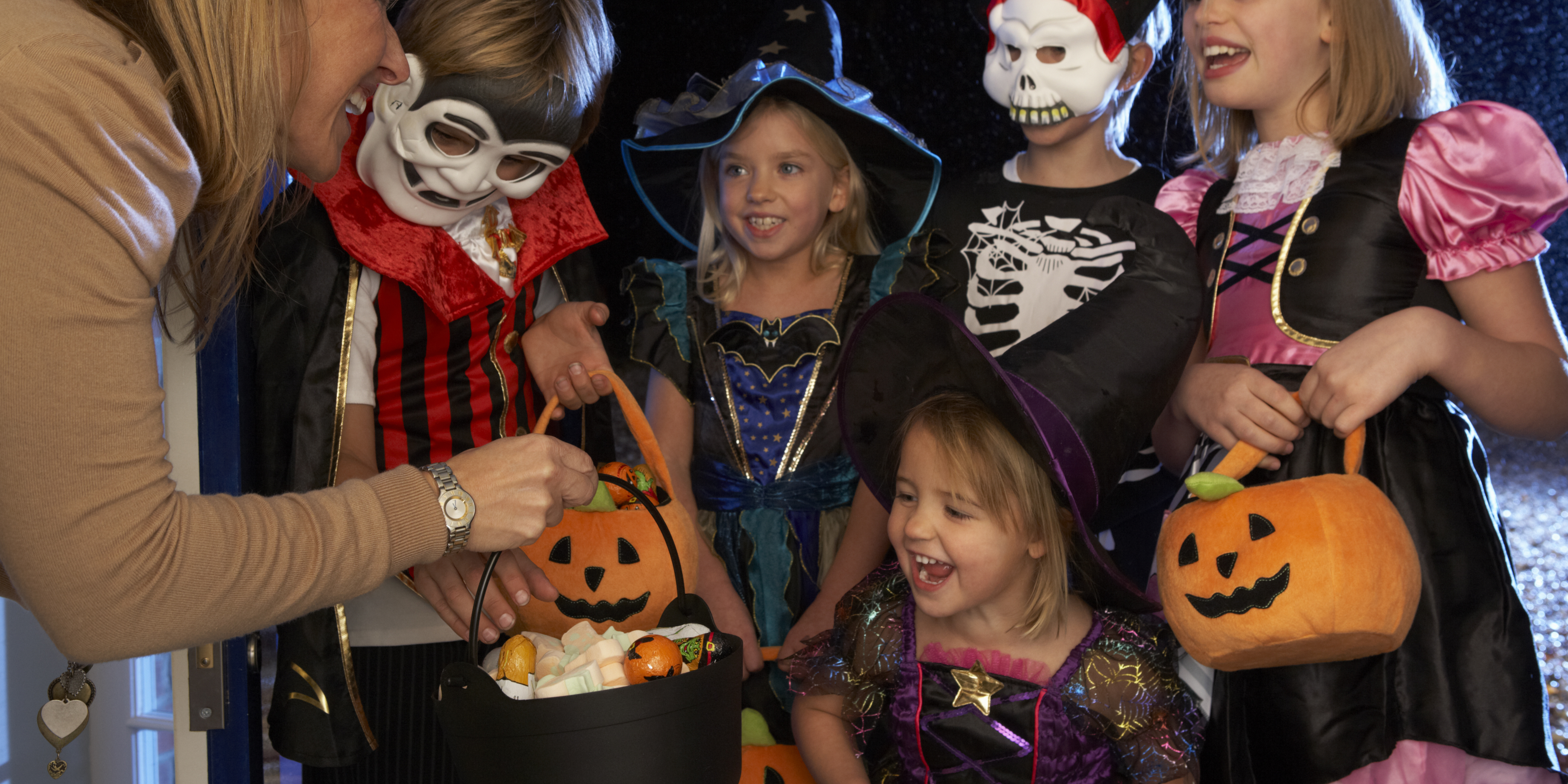 Group of children in Halloween costumes smiling as they receive candy from an adult, symbolizing co-parenting cooperation and family fun during the holidays.