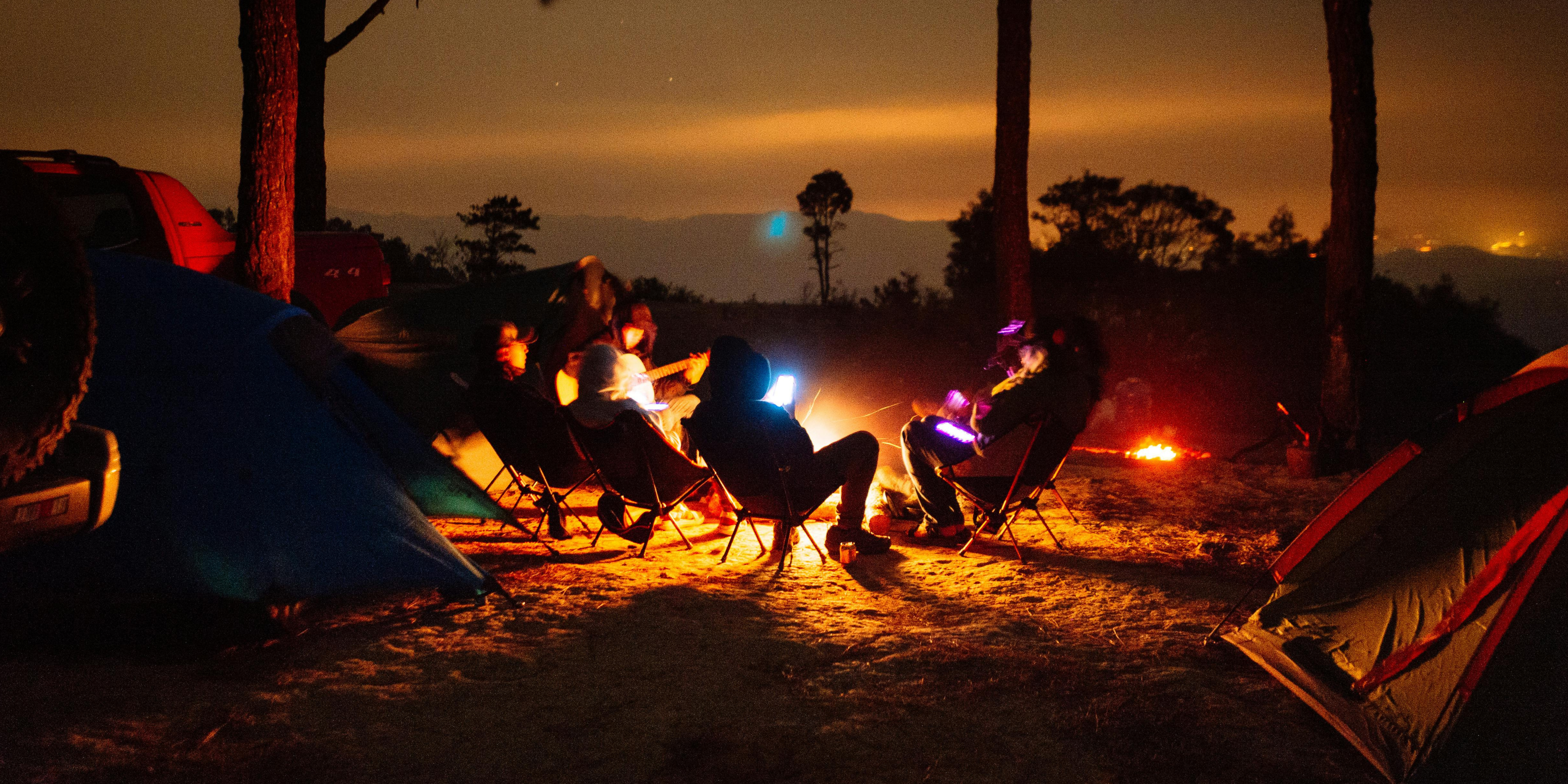 Family sitting around a campfire at night during a summer camping trip, symbolizing co-parenting coordination, planning, and connection during summer break after divorce.