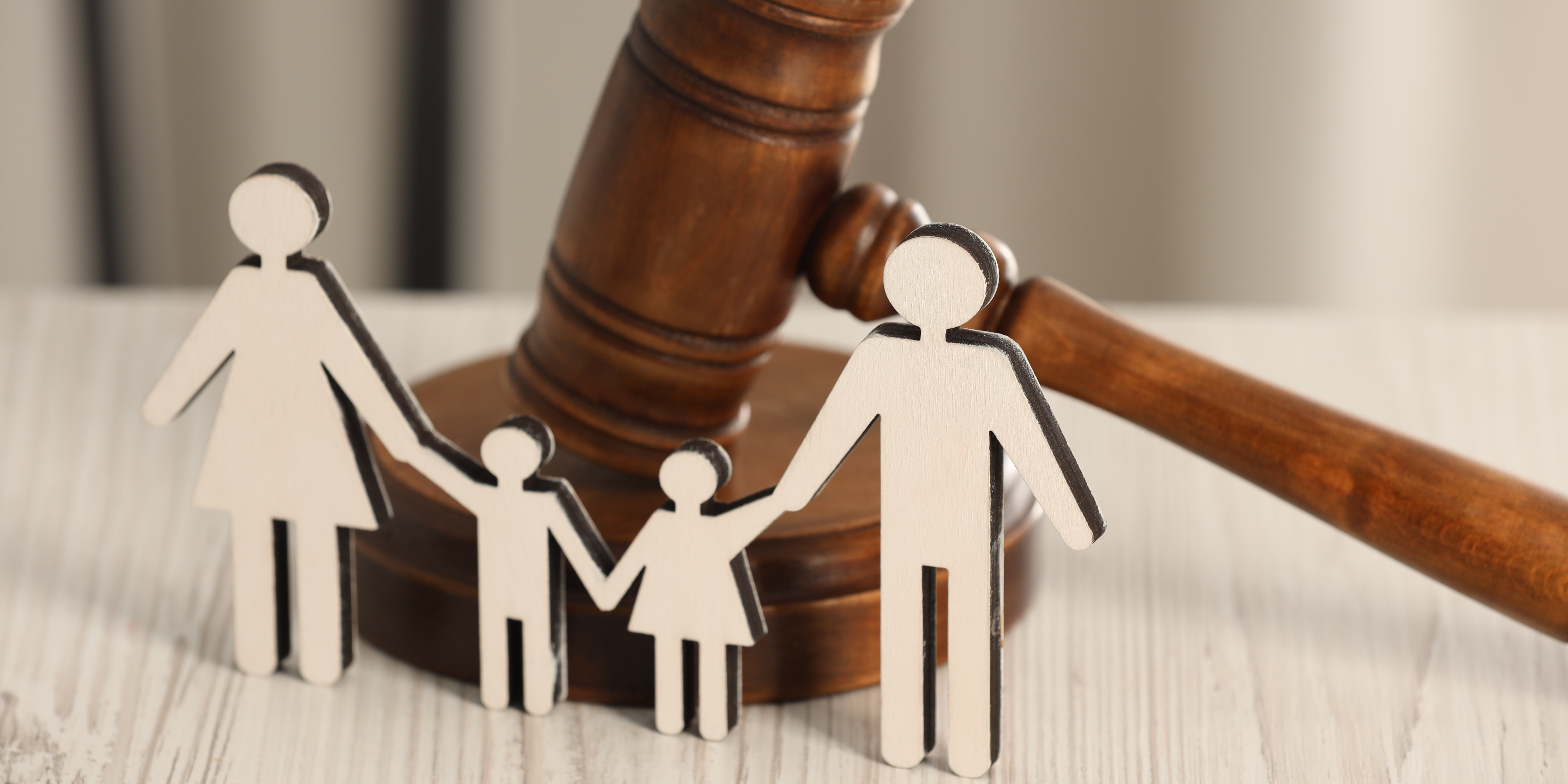 A wooden gavel behind paper cutouts of a family holding hands, symbolizing family law and co-parenting decisions.