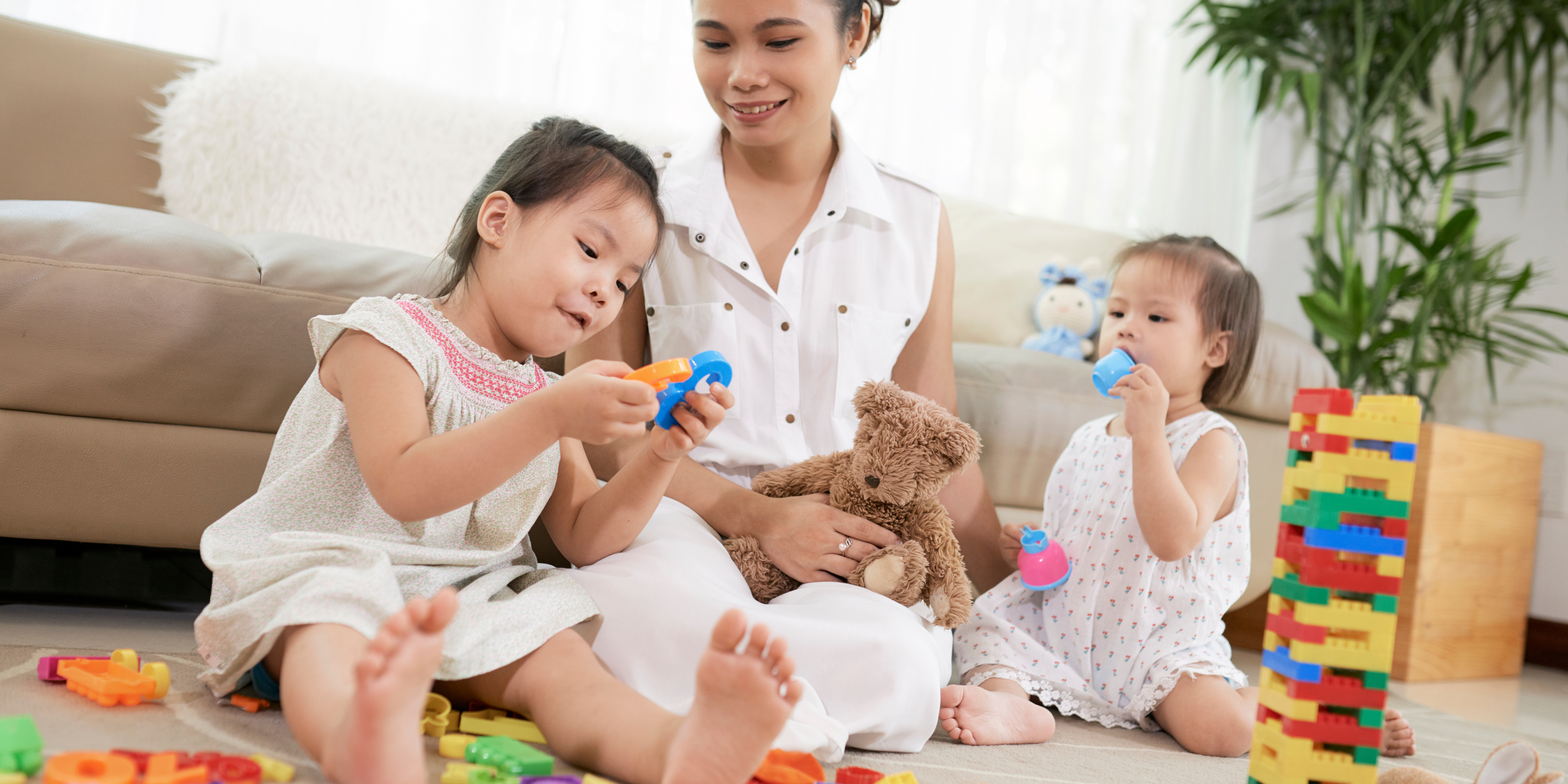 A parent sitting on the floor with two young children playing with toys, representing the stay-at-home parenting role.