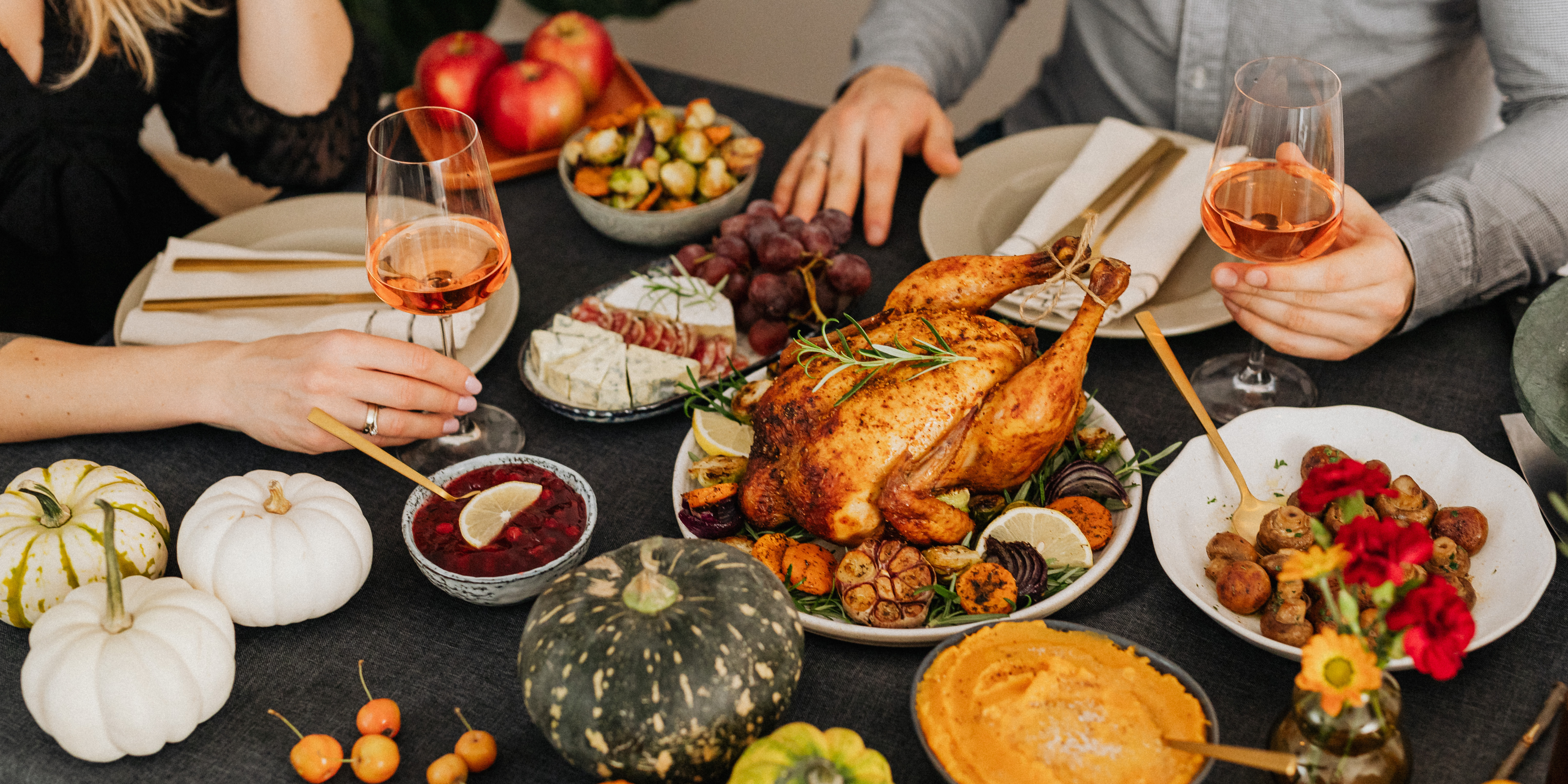 Close-up of a festive Thanksgiving dinner table with roasted turkey, autumn decorations, and two people clinking glasses, symbolizing co-parenting and shared family holidays.