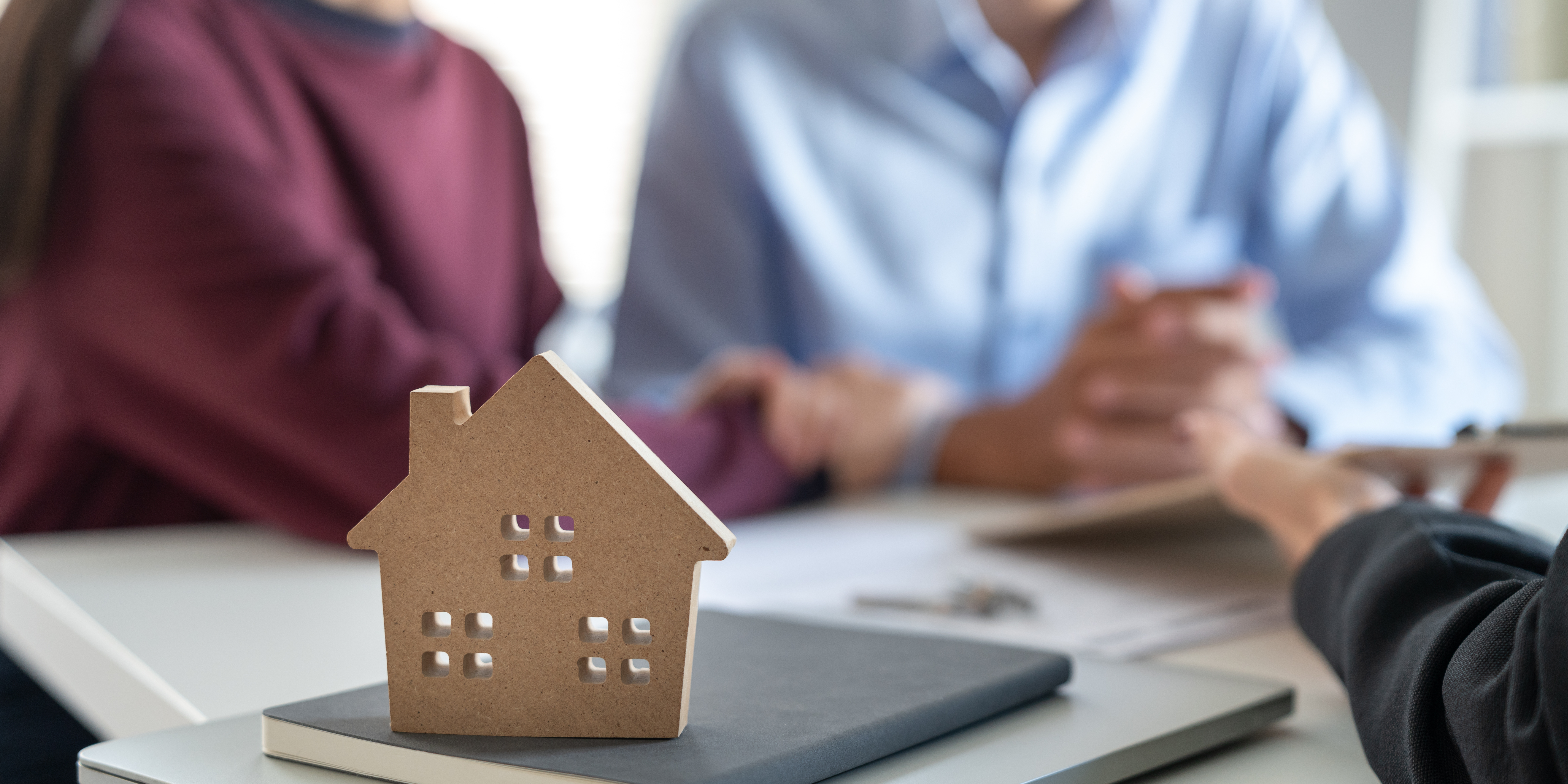 A small model house on a desk with a couple meeting an advisor in the background, symbolizing estate planning after divorce.