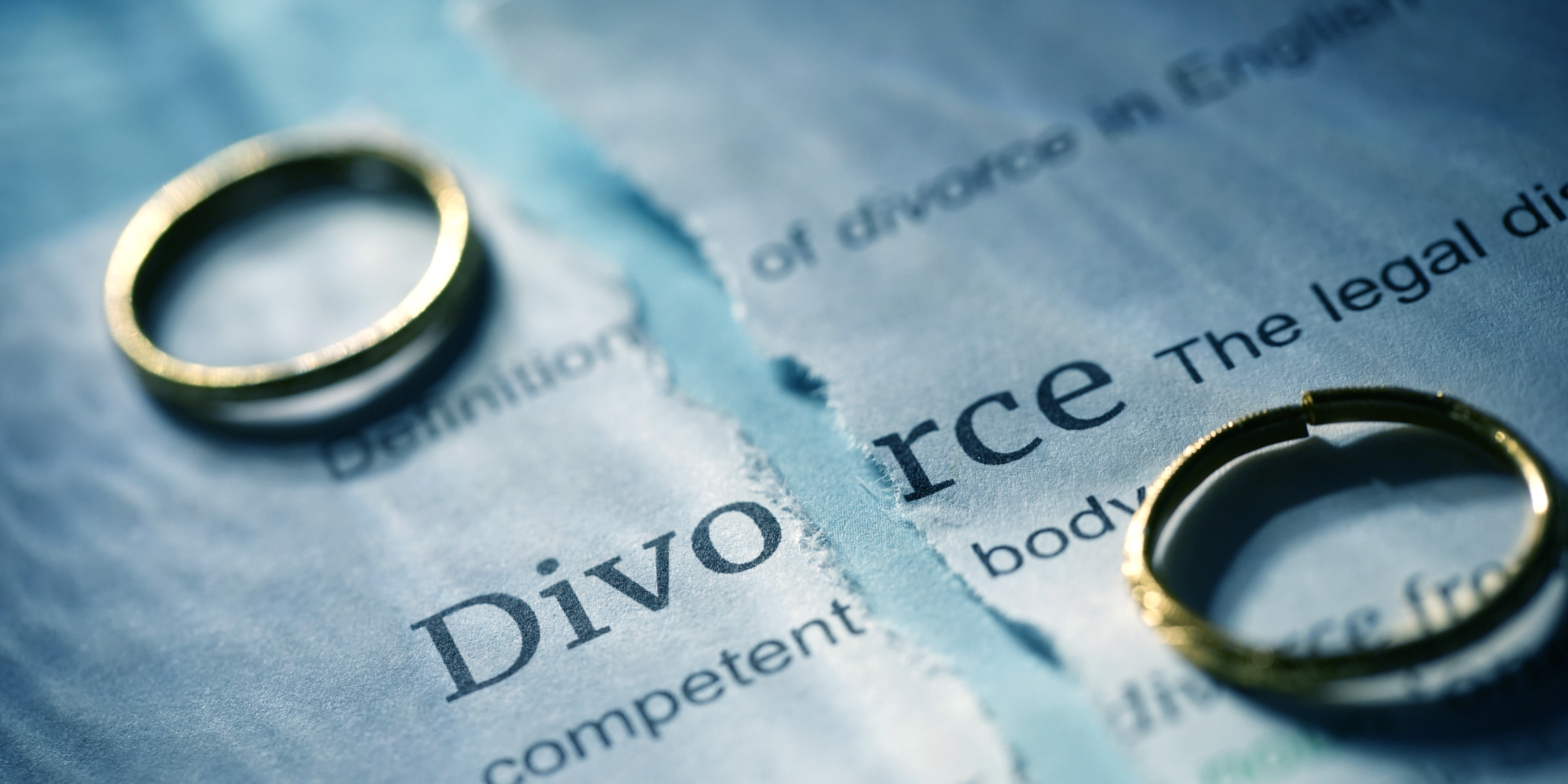 Two wedding rings resting on a torn divorce document, symbolizing separation and the beginning of the divorce process.